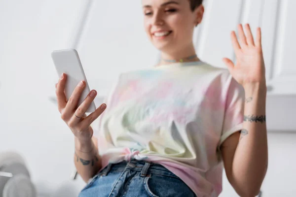Низький кут зору щасливої татуйованої жінки махає рукою під час відеодзвінка на смартфон — стокове фото