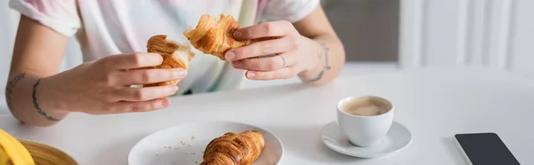 Vista parcial de la mujer sosteniendo delicioso croissant cerca de la taza de café, bandera - foto de stock
