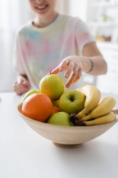 Foco seletivo de tigela com frutas frescas perto de mulher cortada sorrindo no fundo borrado — Fotografia de Stock