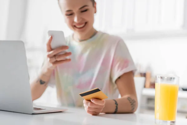 Blurred woman with credit card and smartphone near laptop and glass of orange juice - foto de stock