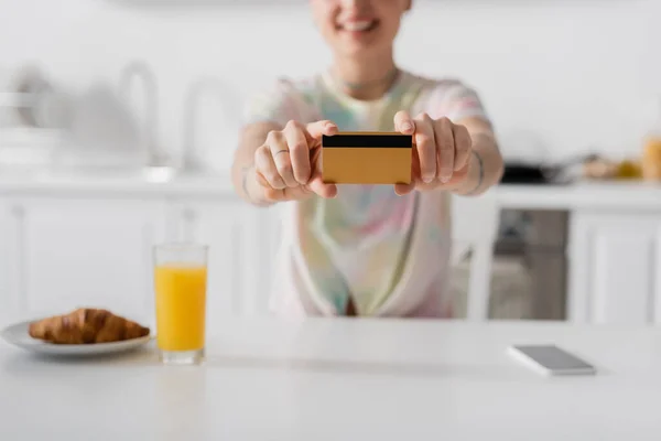 Vista ritagliata della donna offuscata che mostra la carta di credito vicino a succo d'arancia, croissant e smartphone — Foto stock