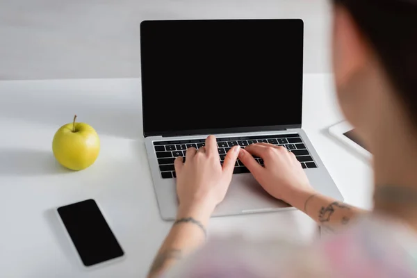 Vista cortada de mulher desfocada digitando no laptop perto de smartphone com tela em branco e maçã madura — Fotografia de Stock