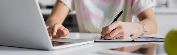 Visão parcial da mulher escrevendo no notebook ao usar laptop em primeiro plano desfocado, banner — Fotografia de Stock