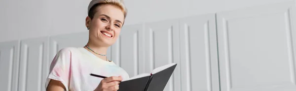 Low angle view of happy woman with trendy hairstyle writing in notebook, banner — Stock Photo