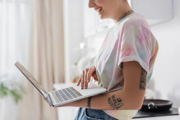 Cropped view of smiling tattooed woman holding laptop in kitchen — стоковое фото
