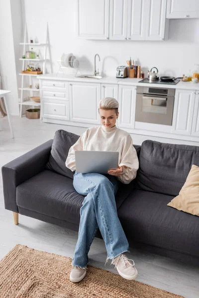 High angle view of trendy woman using laptop on sofa in modern open plan kitchen — Foto stock