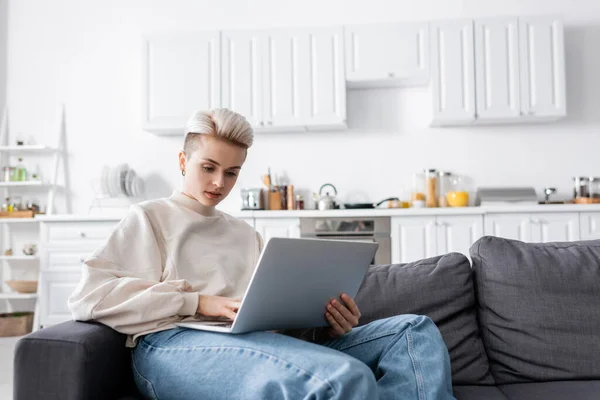 Young woman using laptop on couch in open plan kitchen — Stockfoto