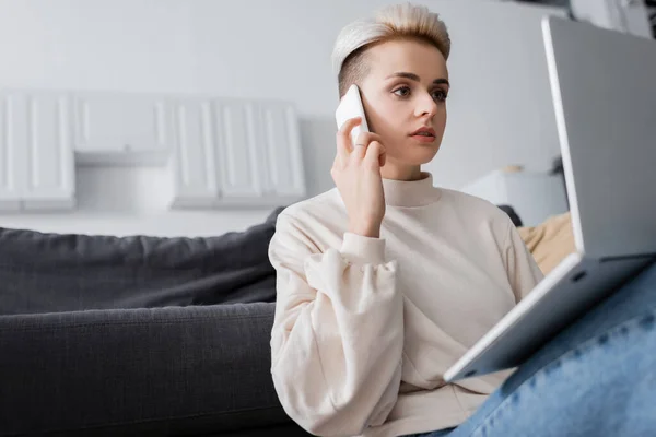 Woman with trendy hairstyle talking on mobile phone near laptop — стоковое фото