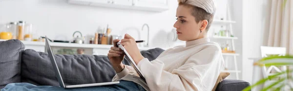 Stylish woman writing in notebook near laptop on couch at home, banner — Fotografia de Stock