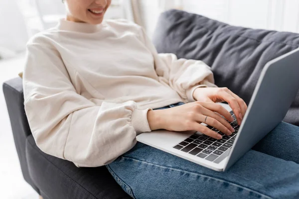 Abgeschnittene Ansicht einer glücklichen Frau, die zu Hause auf dem Sofa auf dem Laptop tippt — Stockfoto