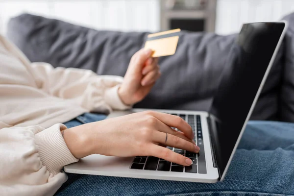 Vista parcial de la mujer que sostiene la tarjeta de crédito y escribir en el ordenador portátil con pantalla en blanco - foto de stock