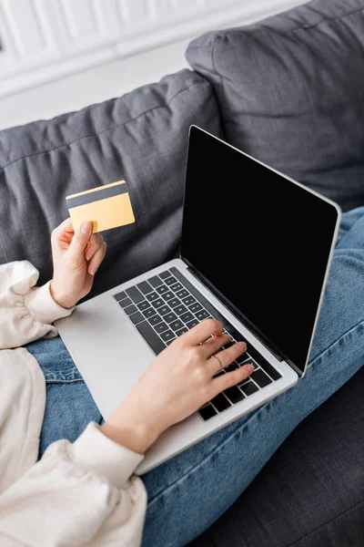 Vista recortada de la mujer con ordenador portátil y tarjeta de crédito en el sofá en casa - foto de stock