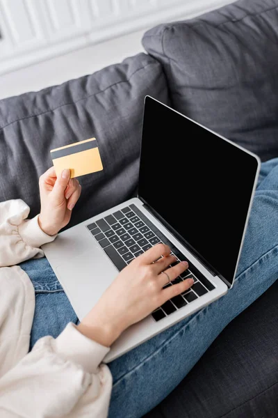 Cropped view of woman with laptop and credit card on couch at home - foto de stock