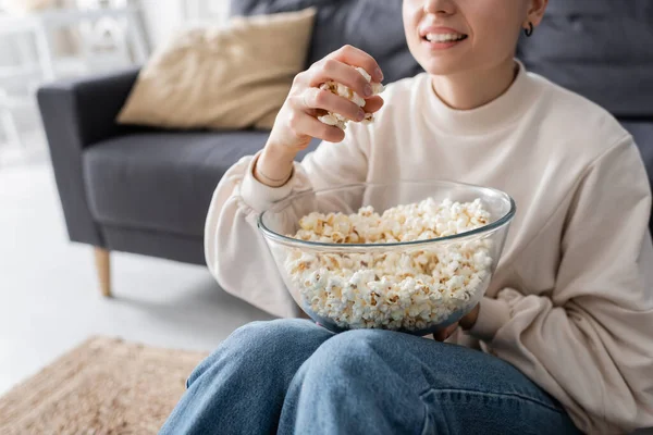 Cropped view of smiling woman with bowl of popcorn watching tv on floor at home — Stock Photo