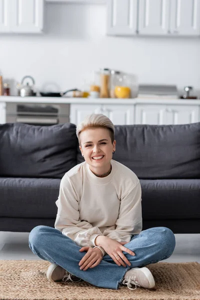 Excited woman sitting on floor with crossed legs and smiling at camera - foto de stock