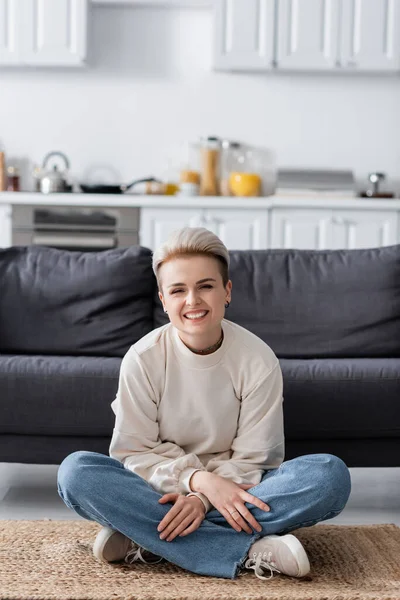 Excited woman sitting on floor with crossed legs and smiling at camera — стоковое фото