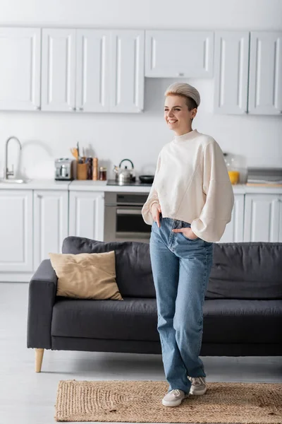 Comprimento total da mulher na moda posando com as mãos em bolsos de jeans na cozinha em plano aberto — Fotografia de Stock