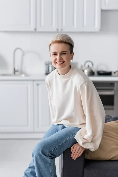 Donna gioiosa con acconciatura alla moda sorridente alla fotocamera a casa — Foto stock