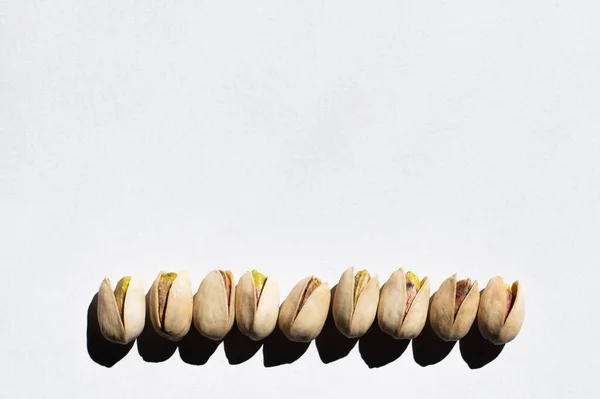 Flat lay view of row with salty cracked pistachios on white background — Stockfoto