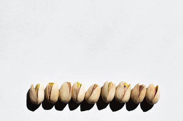 Vista plana de la fila con pistachos salados agrietados sobre fondo blanco - foto de stock