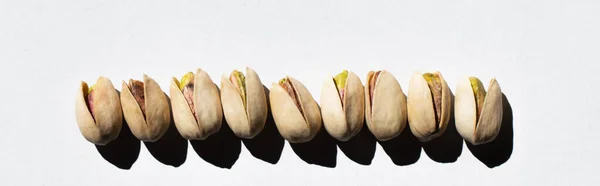 Flat lay view of row with salty cracked pistachios on white, banner — Foto stock