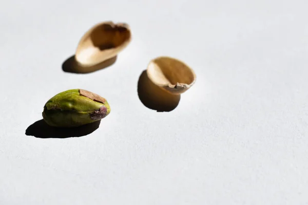 Cracked green and salty pistachio near blurred nutshells on white background — Photo de stock