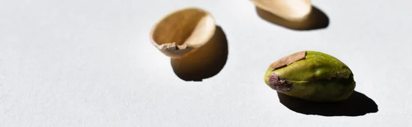 Cracked green and salty pistachio near blurred nutshells on white background, banner — стоковое фото