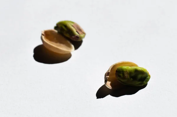 Cracked green and salty pistachios near blurred nutshells on white background — Stock Photo