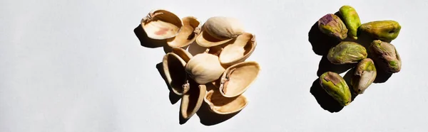 Vista superior de pistachos verdes y salados agrietados cerca de cáscaras de nuez sobre fondo blanco, pancarta — Stock Photo