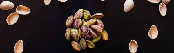 Vista dall'alto di gusci di noce moscata e pistacchi salati isolati su nero, banner — Foto stock