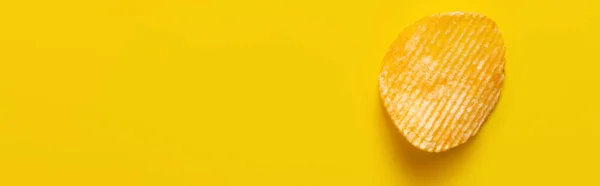 Top view of single wavy and salty potato chip on yellow, banner - foto de stock