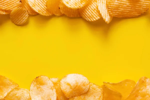 Flay lay view of different salty and wavy potato chips on yellow - foto de stock