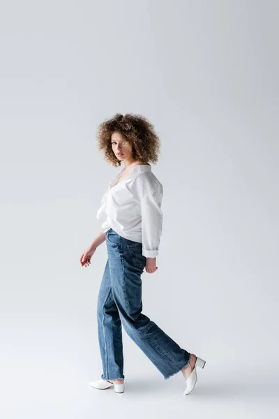 Femme à la mode en jeans marchant sur fond blanc — Photo de stock