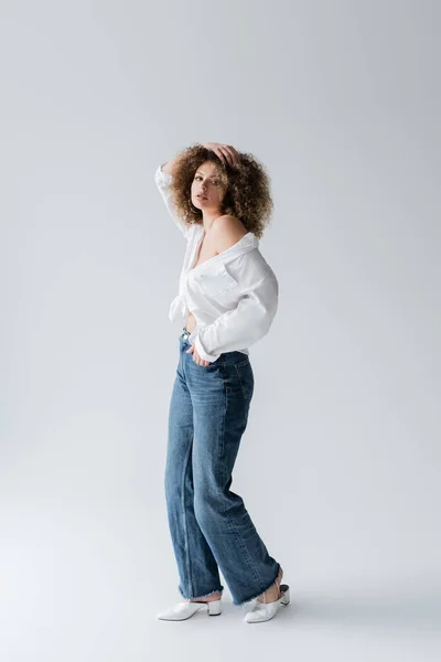 Comprimento total de mulher elegante segurando a mão no bolso de jeans no fundo branco — Fotografia de Stock