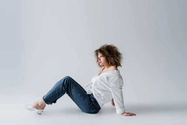 Стильна модель в джинсах сидить на білому тлі — стокове фото