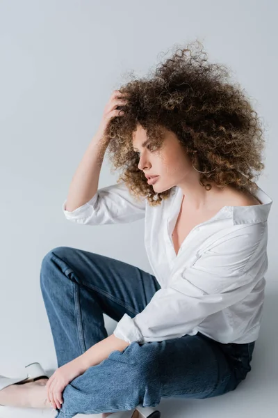 Jolie femme bouclée en chemisier touchant les cheveux sur fond blanc — Photo de stock