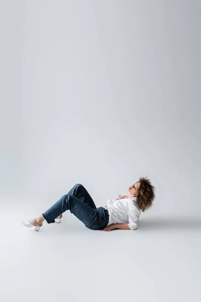 Curly woman in jeans lying on white background — Stock Photo