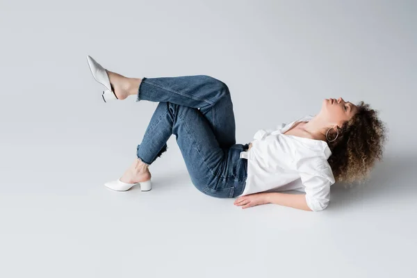 Mulher elegante em jeans e blusa deitada no fundo branco — Fotografia de Stock