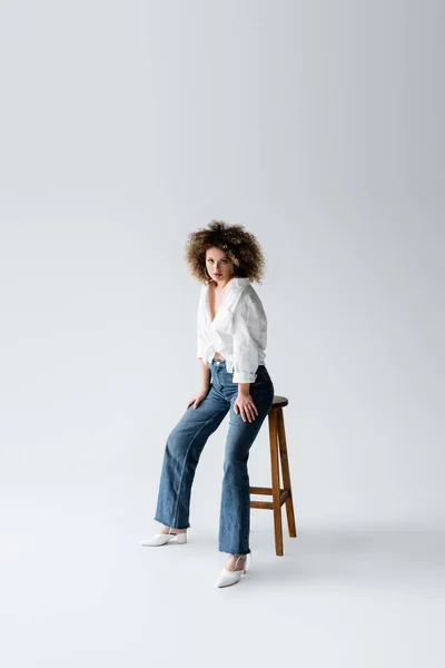 Stilvolles Modell in Bluse posiert in der Nähe Stuhl auf weißem Hintergrund — Stockfoto