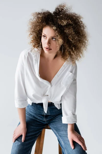 Retrato de mujer rizada elegante sentada en silla aislada en blanco - foto de stock