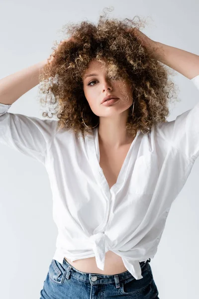 Lockiges junges Model in Bluse, das die Haare isoliert auf Weiß berührt — Stockfoto