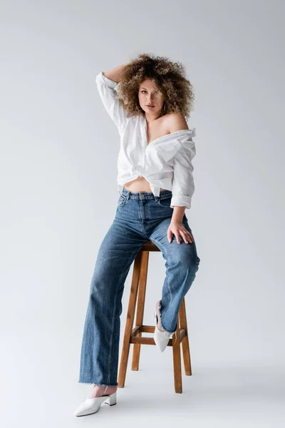 Trendy Modell in Bluse sitzt auf Stuhl auf weißem Hintergrund — Stockfoto