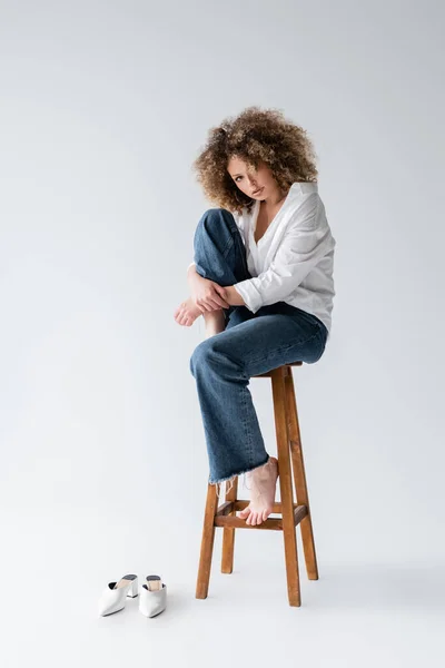 Pretty barefoot model sitting on chair on white background — Stock Photo