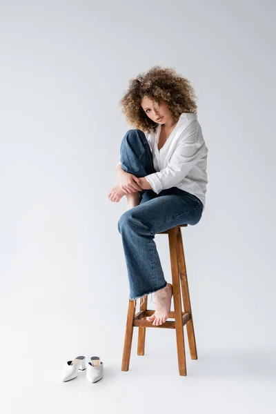 Modelo bastante descalzo sentado en la silla sobre fondo blanco - foto de stock