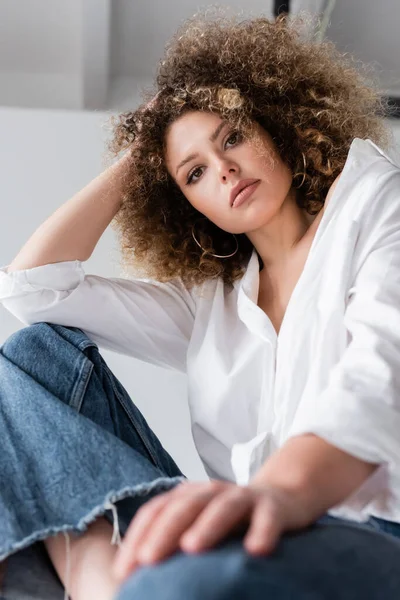 Visão de baixo ângulo do modelo encaracolado na blusa olhando para a câmera no fundo branco — Fotografia de Stock