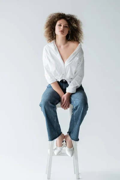 Stylish curly woman in blouse sitting on chair on white background — Stock Photo