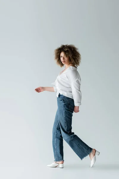 Fashionable woman walking and looking at camera on white background — Stock Photo