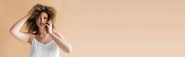 Donna in top bianco toccare i capelli isolati su beige, banner — Foto stock