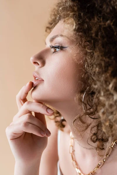 Side view of young curly model touching lip isolated on beige — Stock Photo