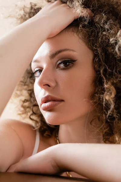 Retrato de modelo joven y elegante tocando el pelo rizado aislado en beige - foto de stock